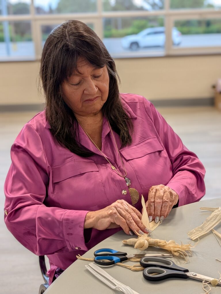 Wisdom in Action, Grandmother Gail Whitlow works on her corn husk doll, Six Nations of the Grand River, August 2026.